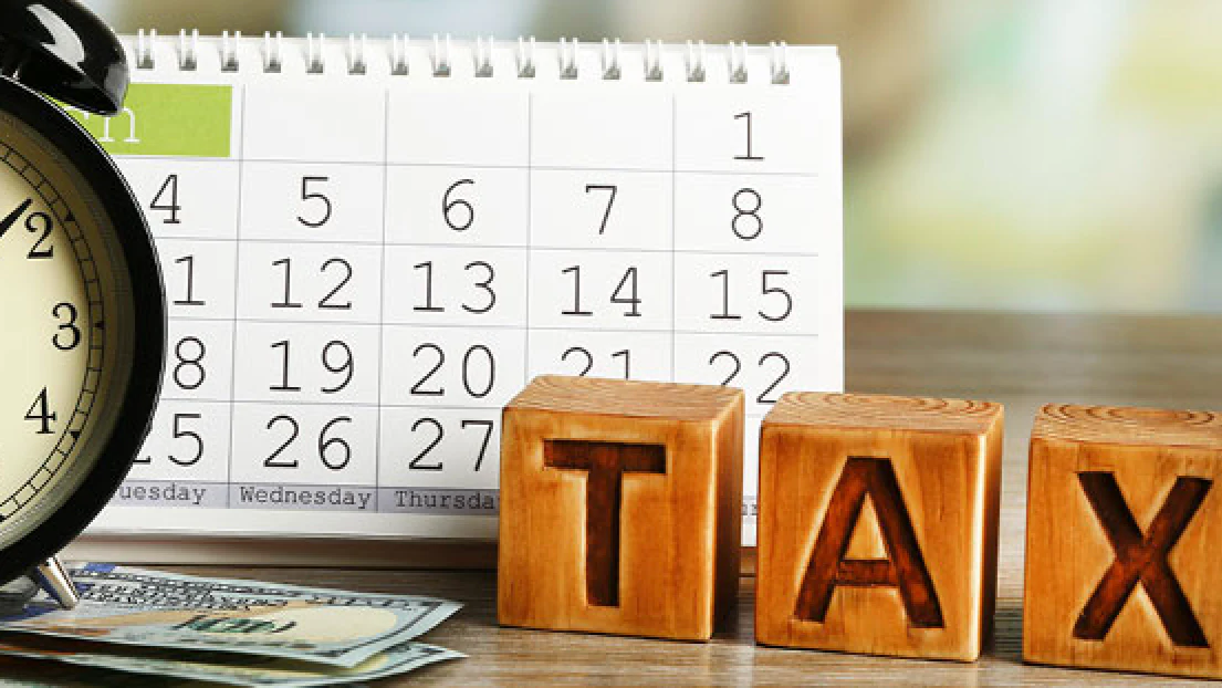 Wooden TAX blocks beside a calendar and an alarm clock