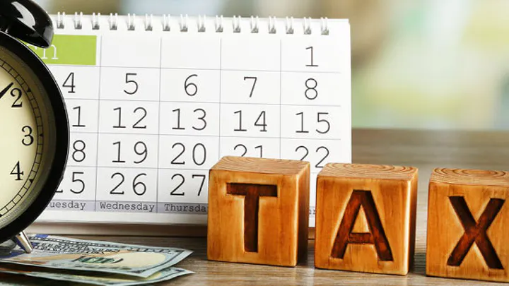 Wooden TAX blocks beside a calendar and an alarm clock